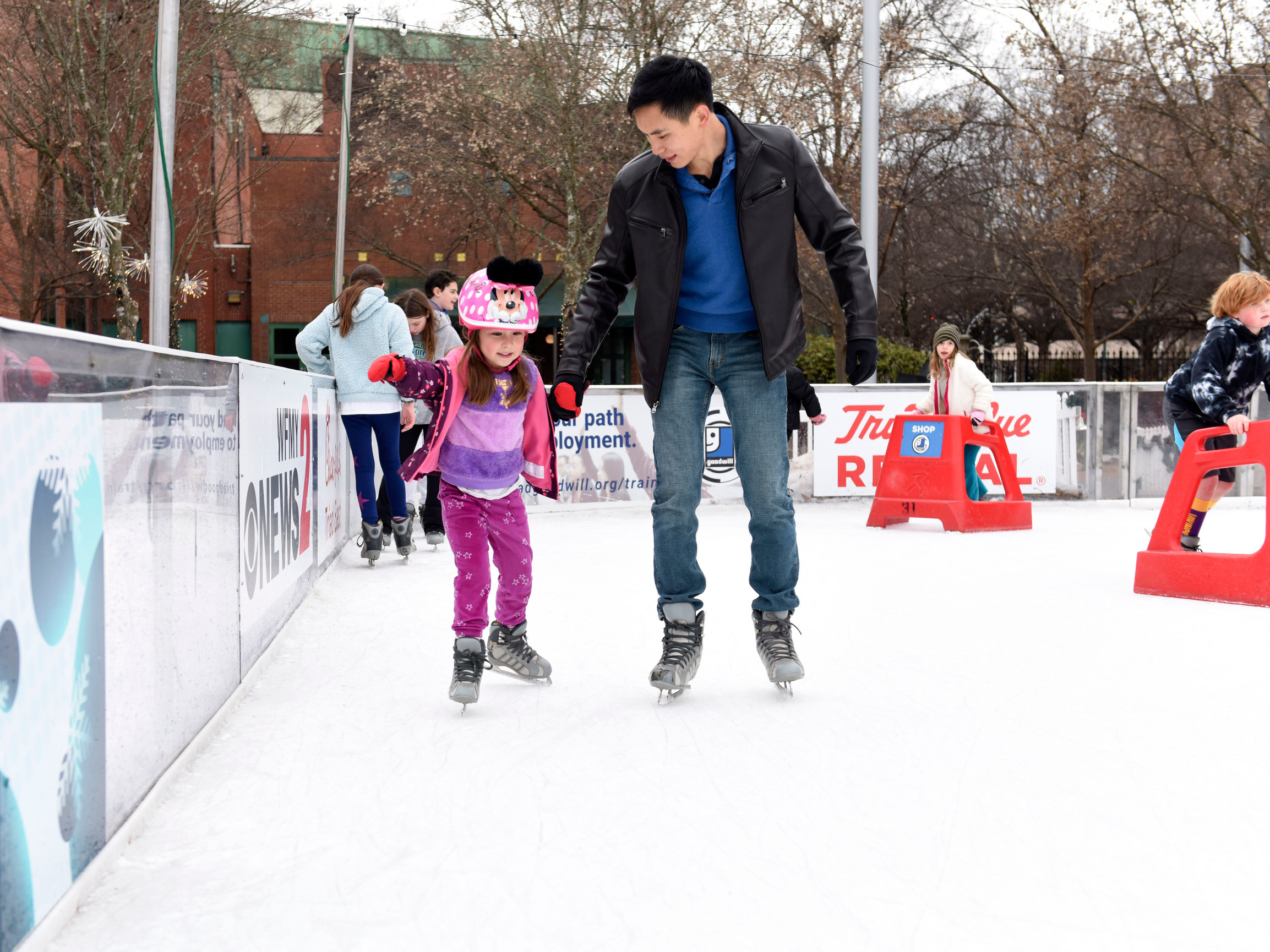 A photo of a Friendly father and his daughter ice skating in 2025.